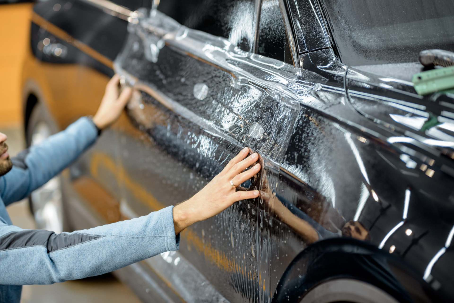 Two installers laying paint protection film along a vehicle's front door and fender