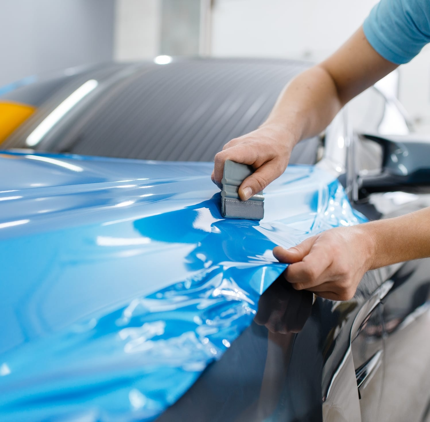 Installer squeegeeing blue film across a car hood