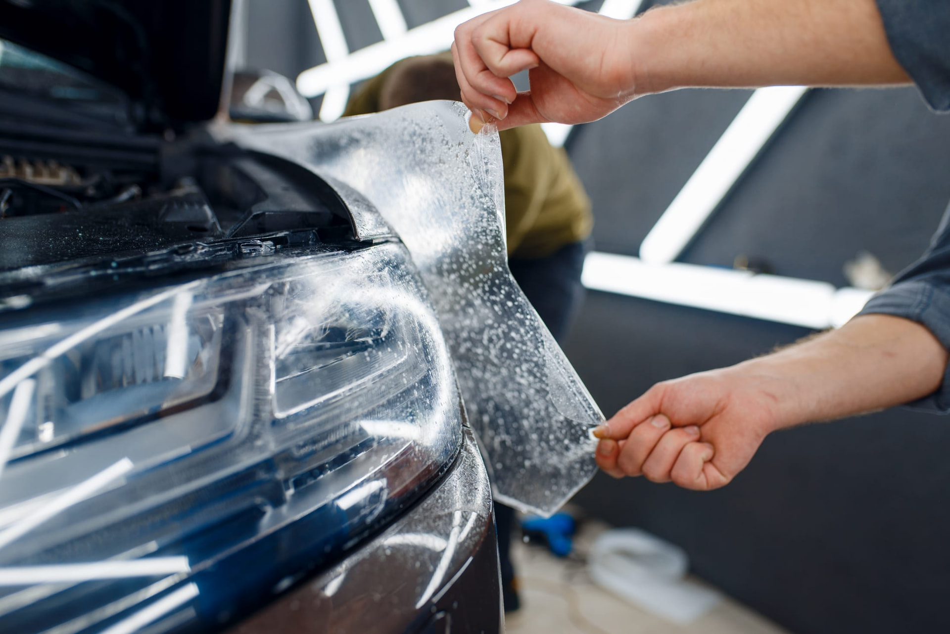 Technician applying paint protection film to a vehicle headlight and front end